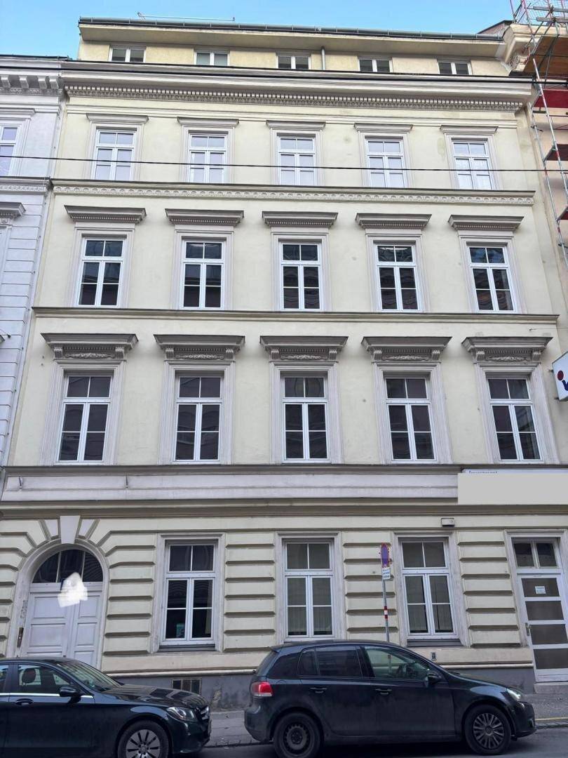 Klassische Fassade eines mehrstöckigen Gebäudes mit symmetrischen Fenstern und geparkten Autos davor.