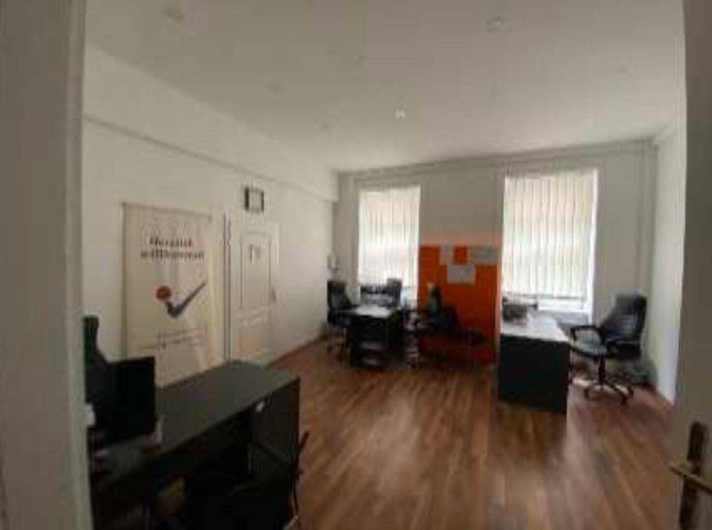Helles Büro mit mehreren Arbeitsplätzen, Holzfußboden und Fenstern mit Jalousien.