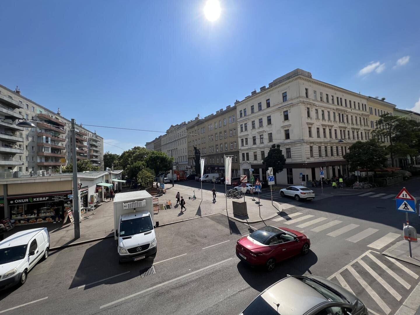 Weitläufiger Blick auf eine städtische Kreuzung mit Gebäuden und Fahrzeugen unter blauem Himmel.