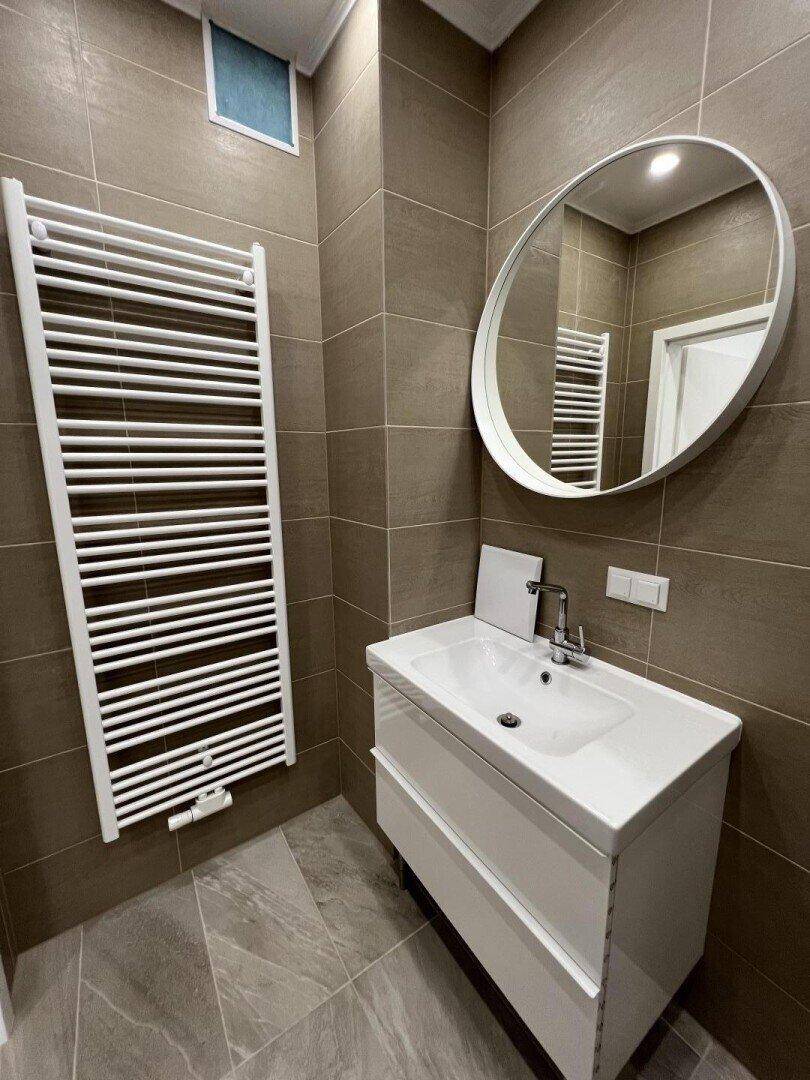 Badezimmer mit modernem Waschbecken, rundem Spiegel und beheiztem Handtuchhalter.