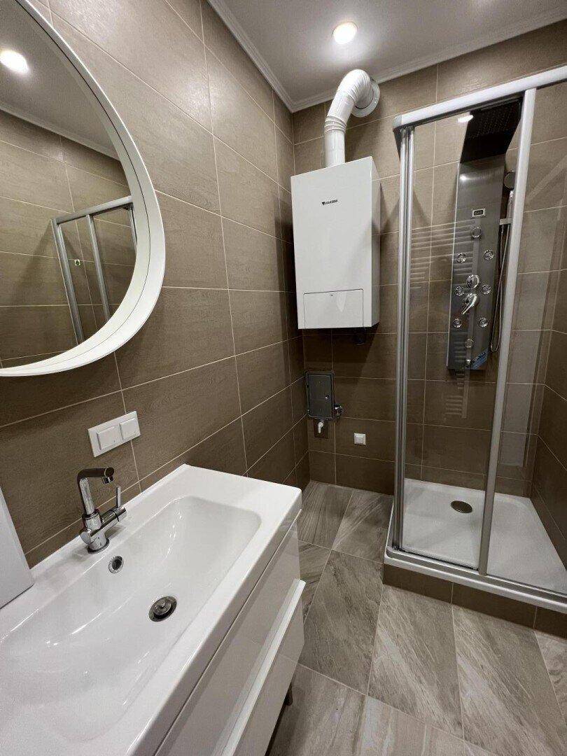 Modernes Badezimmer mit braunen Fliesen, Einzelwaschbecken und einer Duschkabine.