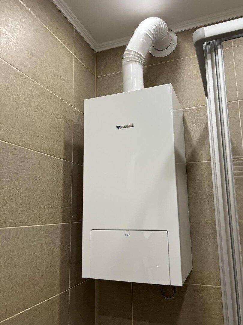 Detailansicht eines Heizkessels an einer gefliesten Wand im Badezimmer.