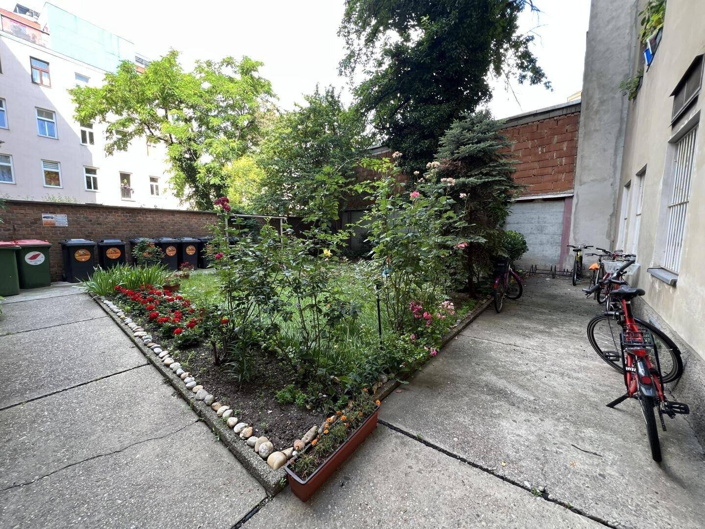 Ruhiger Innenhofgarten mit üppiger Bepflanzung, Rosen und einem Fahrradabstellplatz.