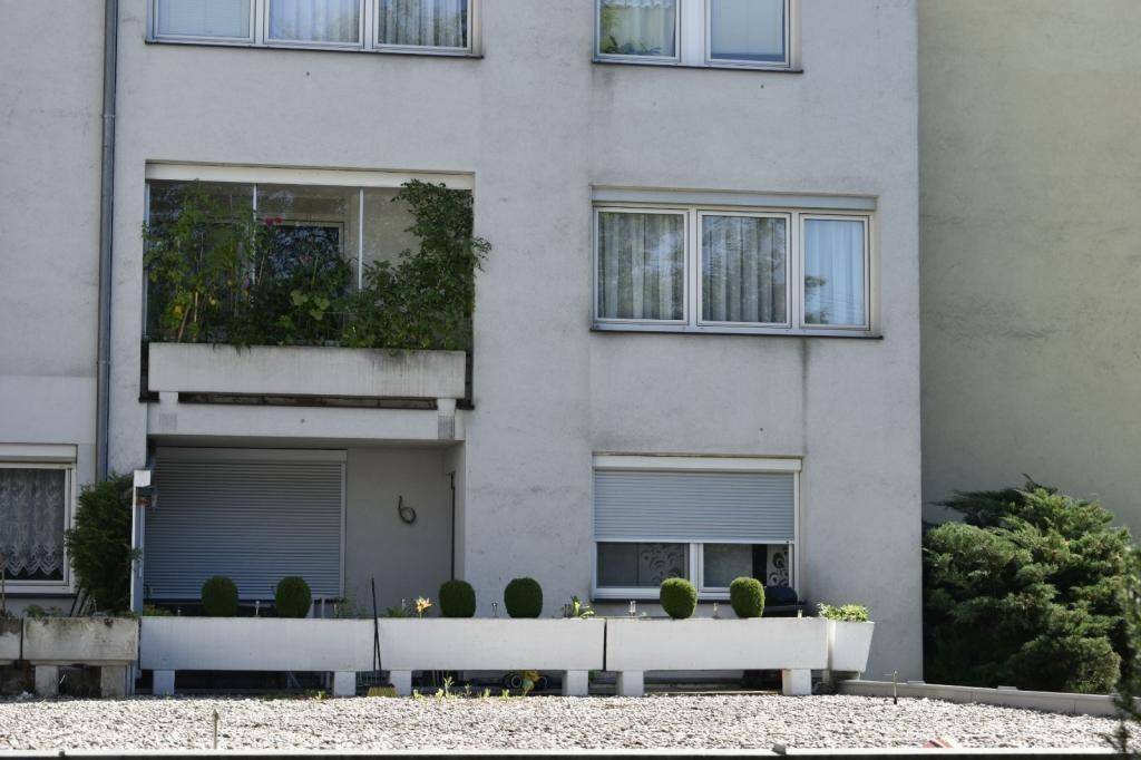 Fassade eines Mehrfamilienhauses mit Balkonen, Rollläden und begrünten Pflanzkübeln.