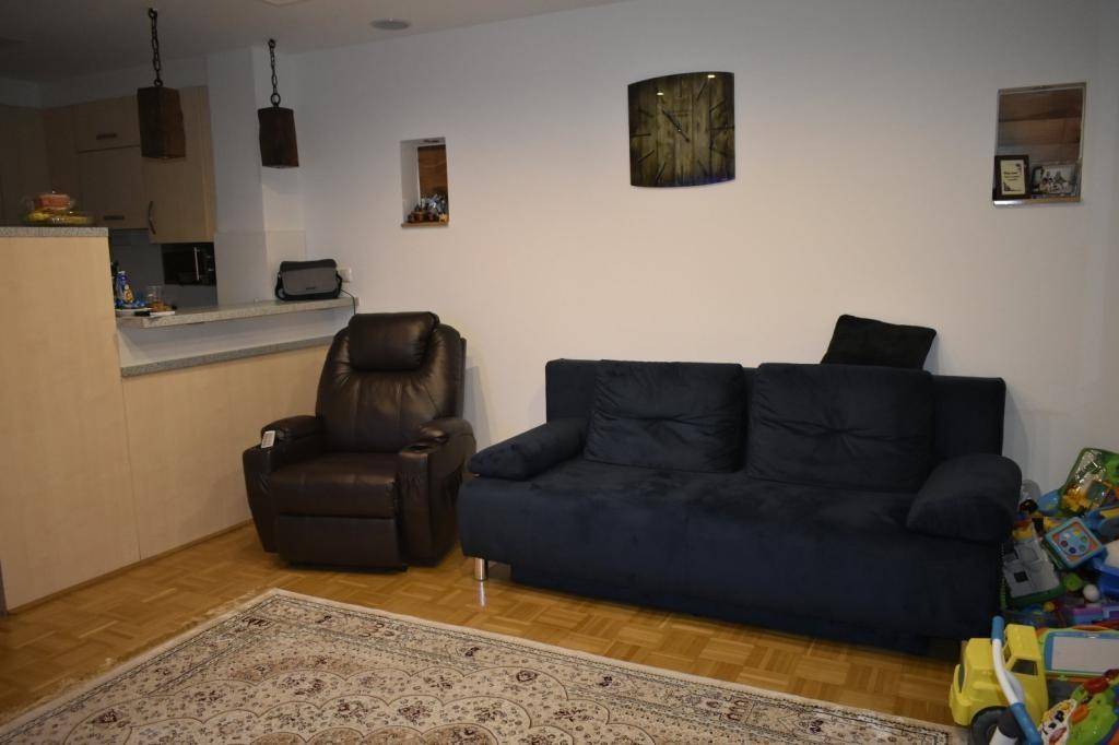 Wohnzimmer mit bequemer Couch, Sessel und Holzboden, offen zum Küchenbereich.