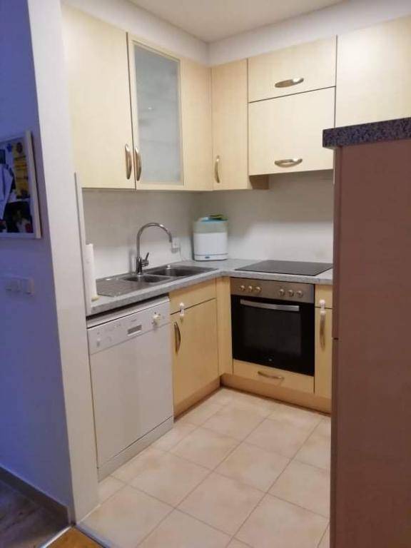 Funktionale Eckküche mit hellen Schränken, integriertem Backofen und Fliesenboden.