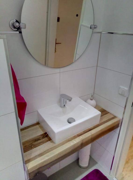 Modernes Badezimmer mit Aufsatzwaschbecken auf Holzplatte und rundem Spiegel.