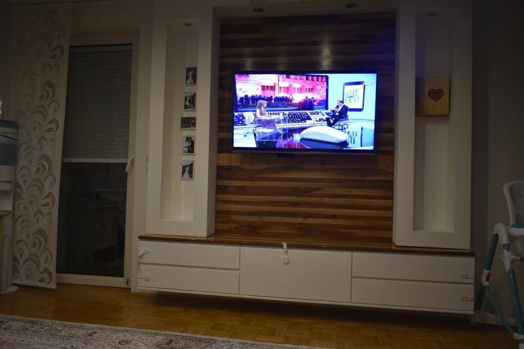 Moderner Wohnbereich mit großem Fernseher an einer Holzvertäfelung und Zugang zum Balkon.