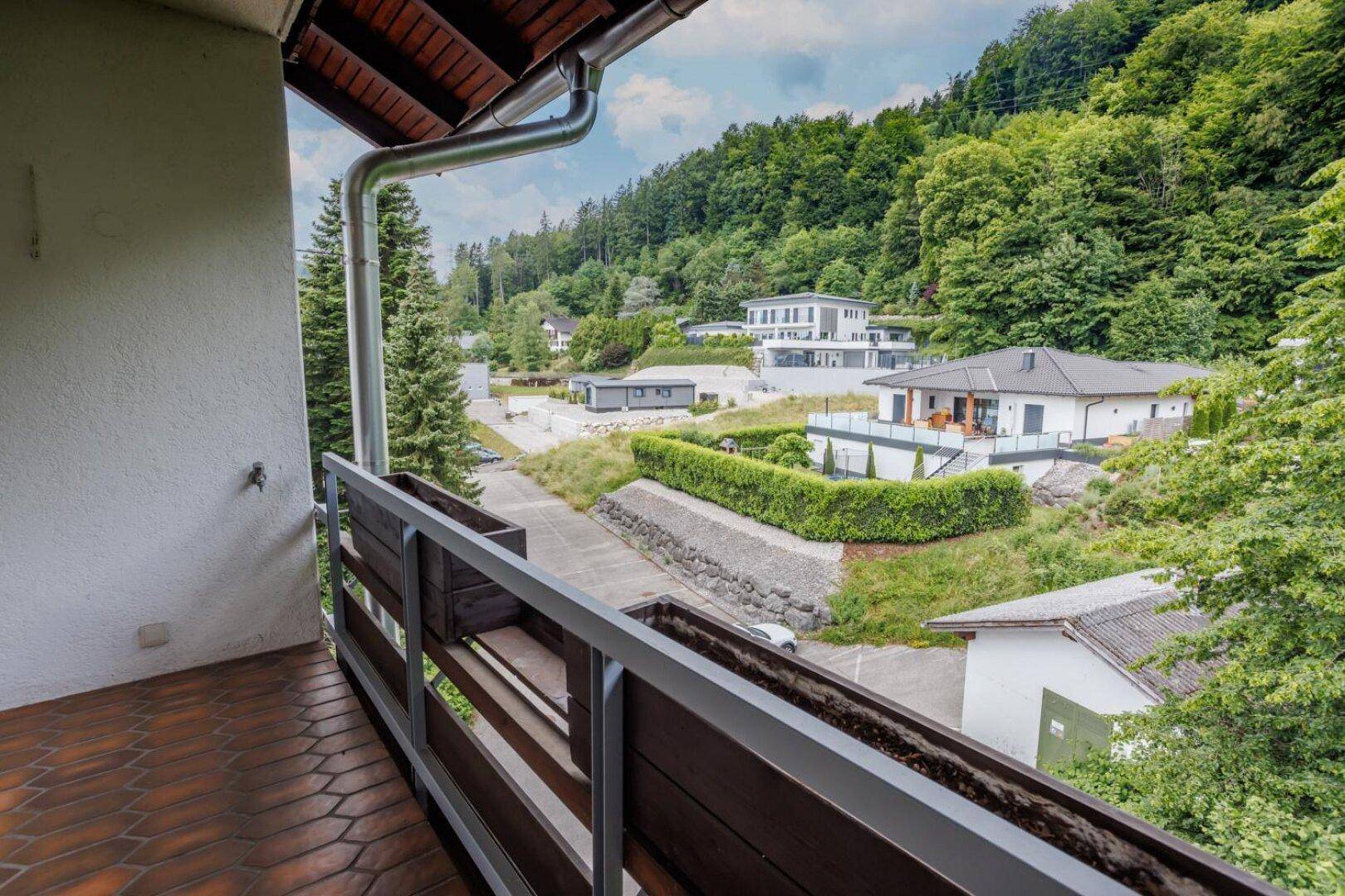Balkon mit Fliesenboden und Blick auf eine grüne Hügellandschaft mit Wohnhäusern.