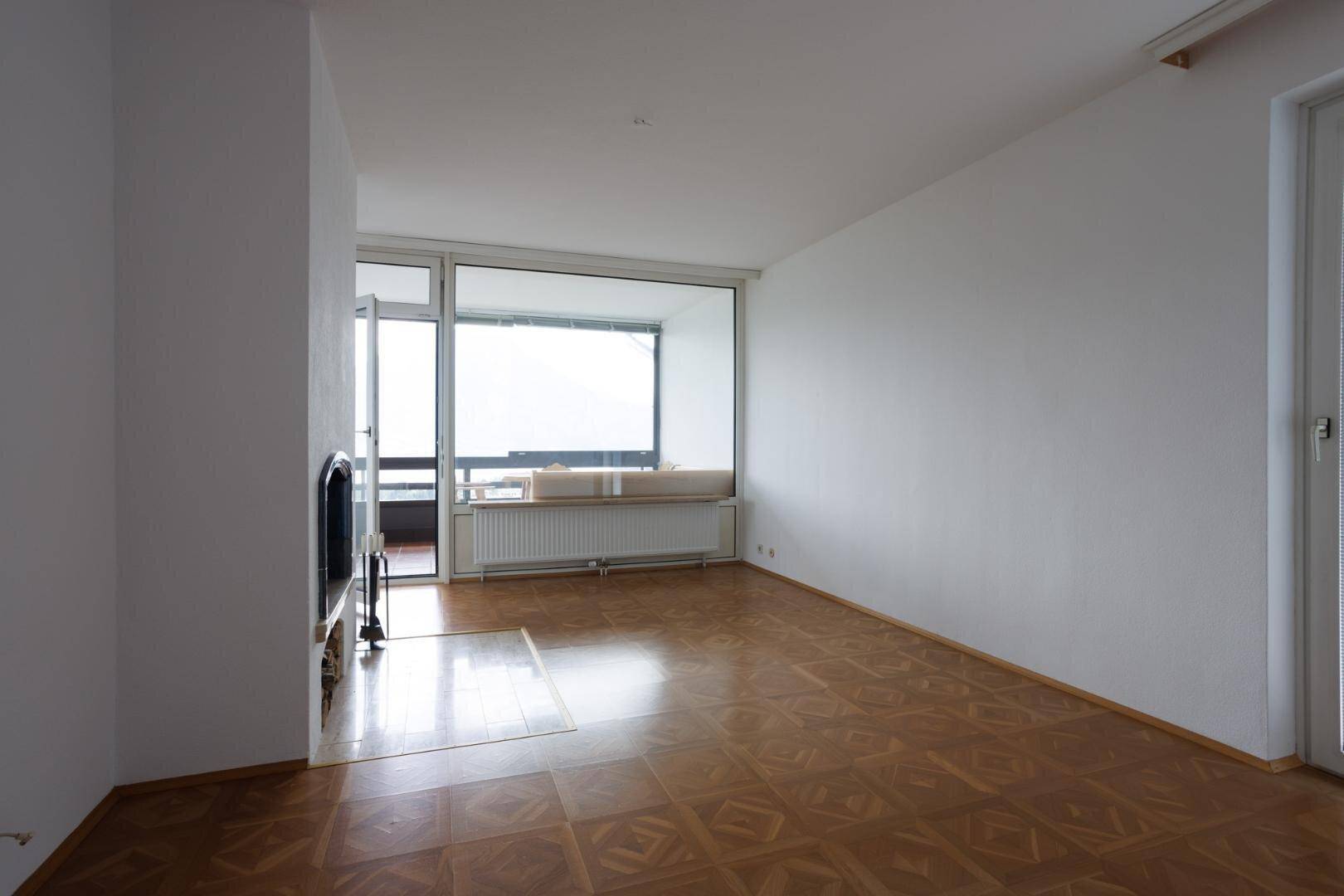 Helles Wohnzimmer mit gemustertem Holzboden, weißen Wänden und großen Fenstern.