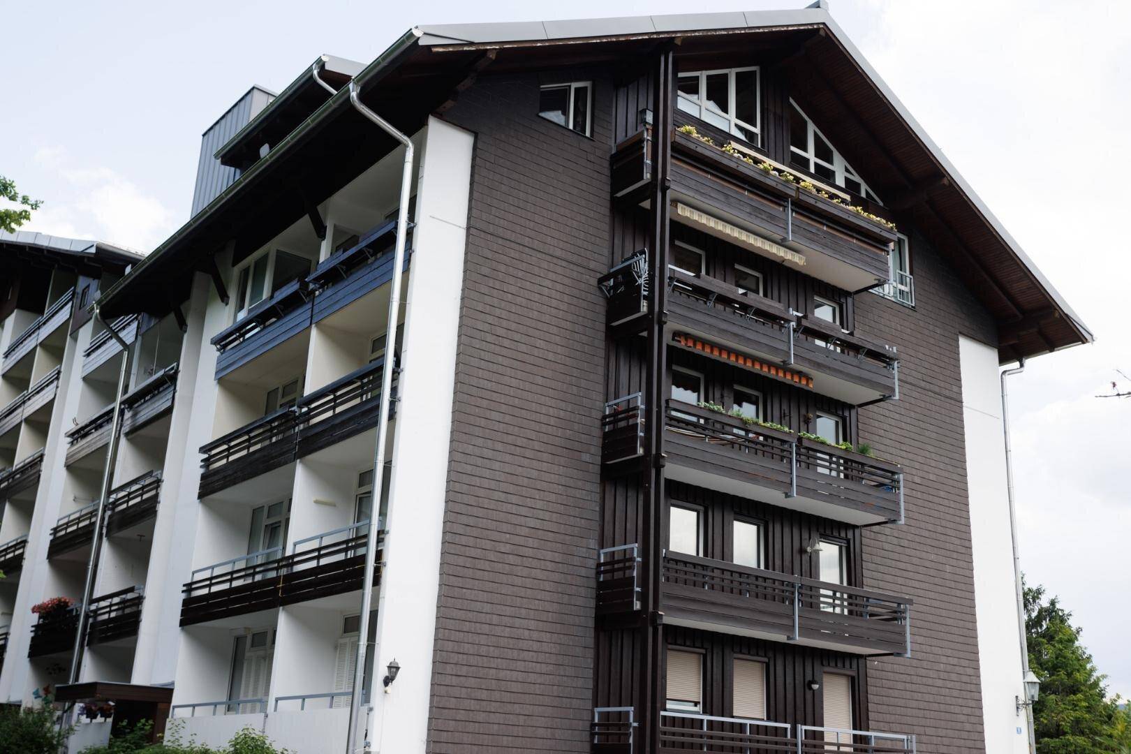 Ansicht des Gebäudes mit dunkler Holzfassade und weißen Akzenten, umgeben von Natur.