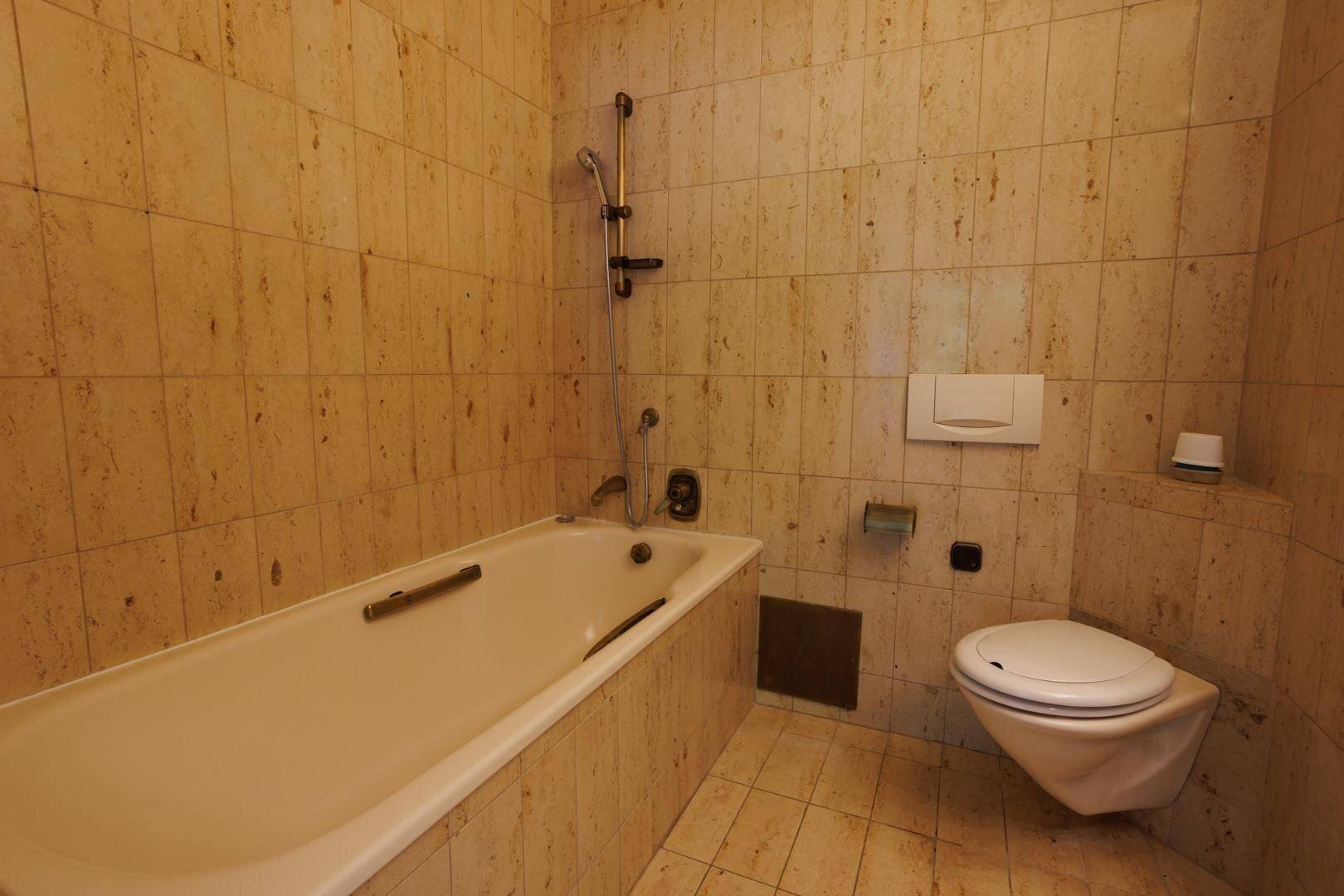 Detailansicht der Badewanne und des wandhängenden WCs in einem gefliesten Badezimmer.