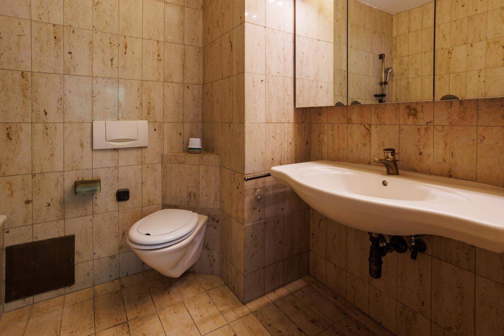 Waschbeckenbereich mit Spiegelschrank und wandhängendem WC in einem gefliesten Badezimmer.