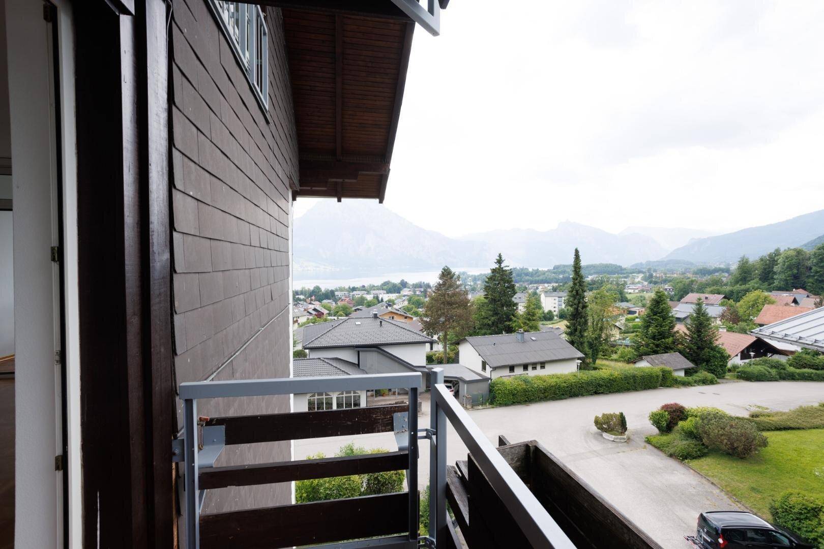 Seitlicher Blick vom Balkon auf die Landschaft mit See, Bergen und benachbarten Häusern.