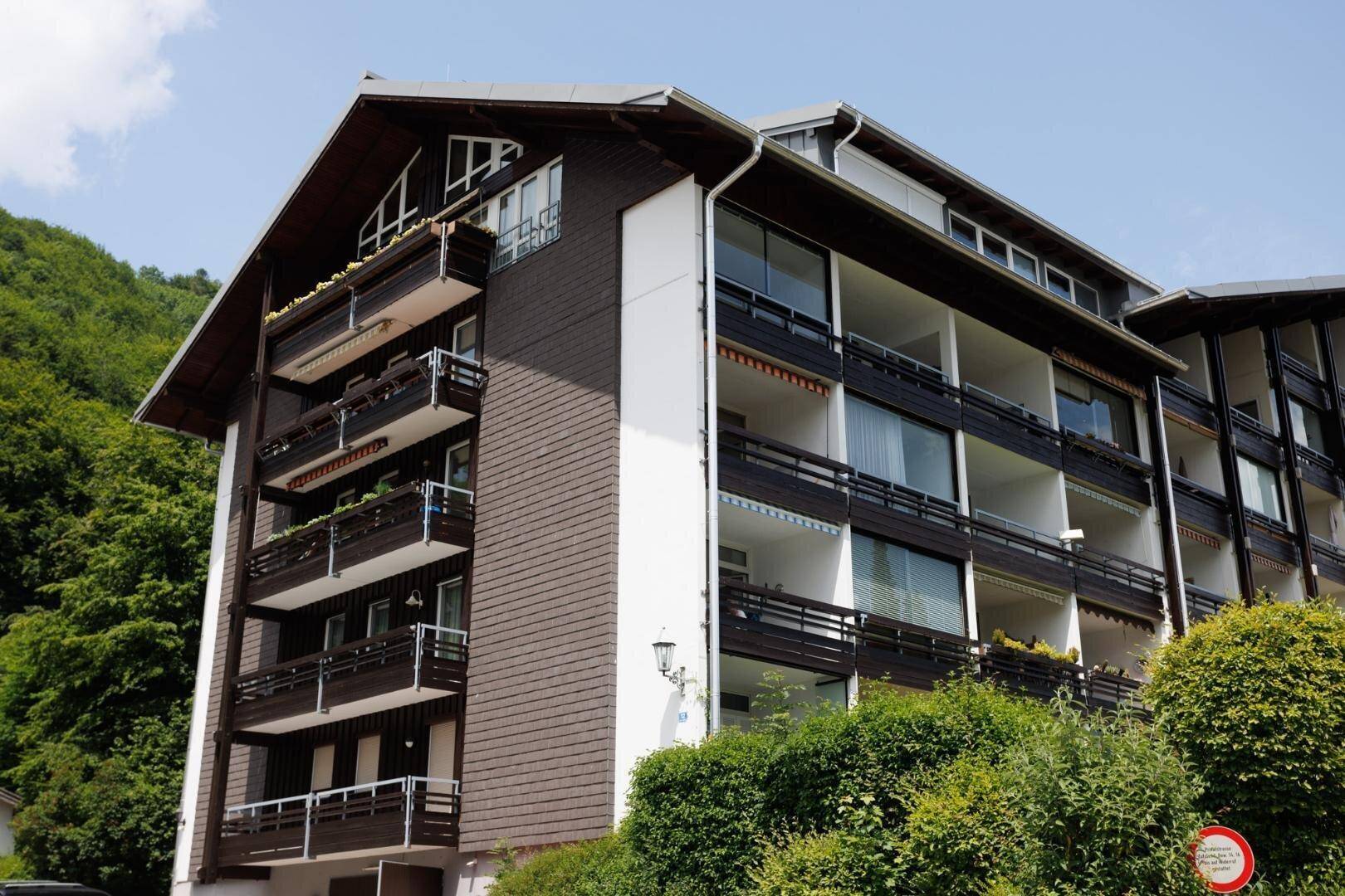 Sonnenbeschienene Fassade des Gebäudes mit vielen Balkonen und grüner Bepflanzung im Vordergrund.