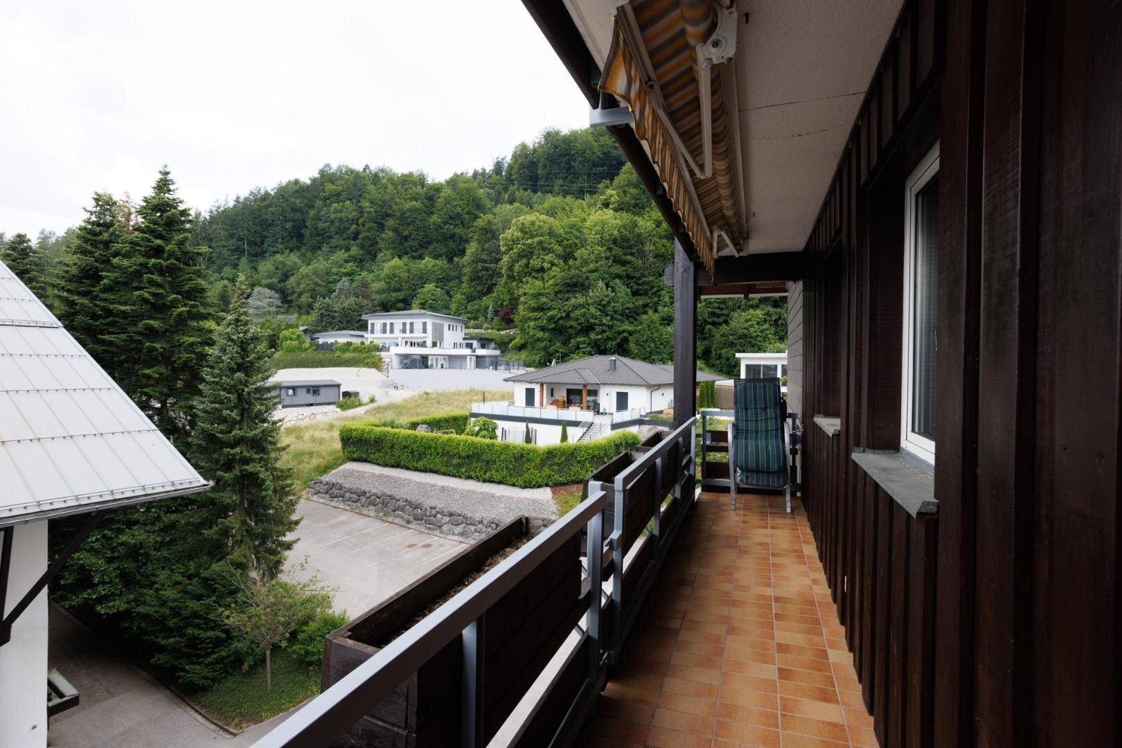 Langer Balkon mit Terrakottafliesen und Holzgeländer, bietet Blick auf die grüne Umgebung.