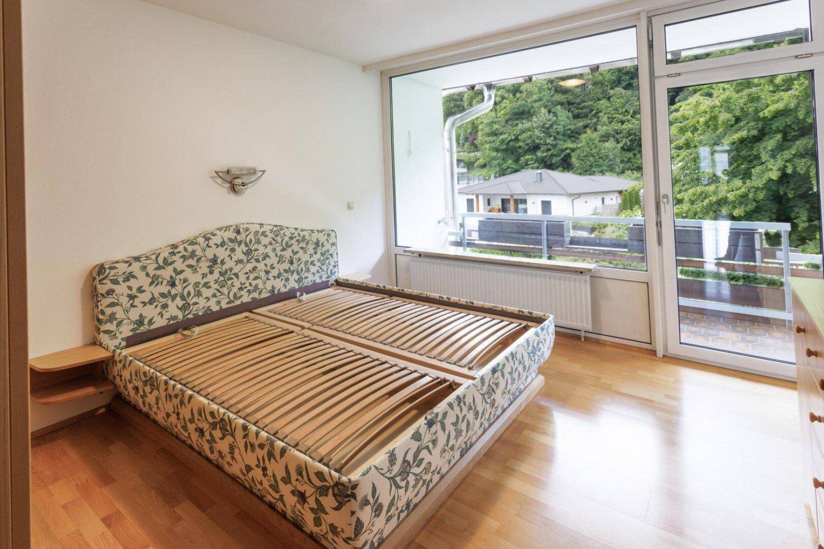 Schlafzimmer mit Holzboden, Bettgestell und großen Fenstern mit Balkonzugang.