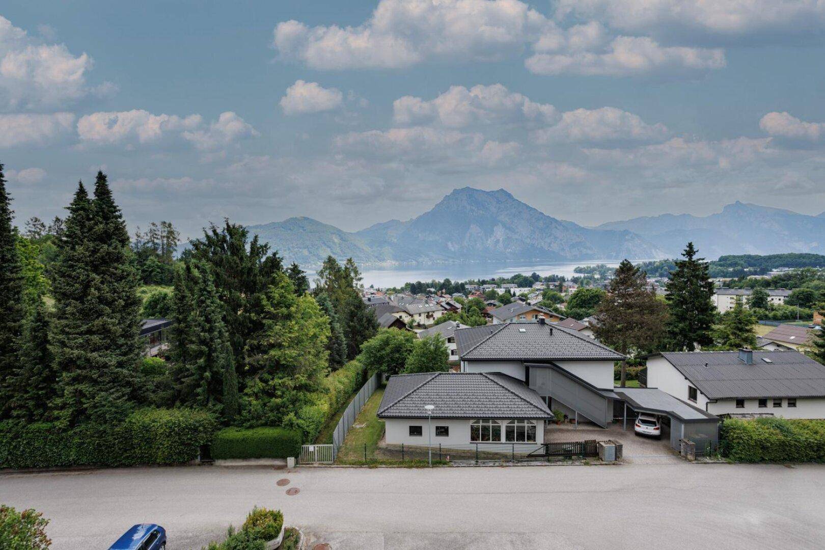 Panoramablick über eine Wohnsiedlung mit See und Bergen im Hintergrund unter bewölktem Himmel.