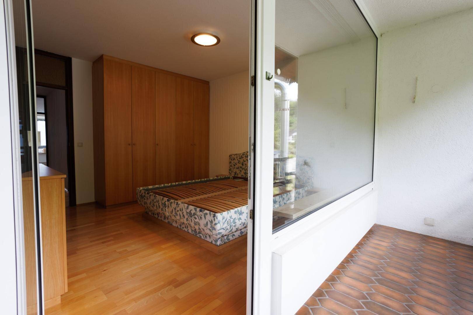 Schlafzimmer mit Holzboden und Blick auf einen überdachten Balkon.