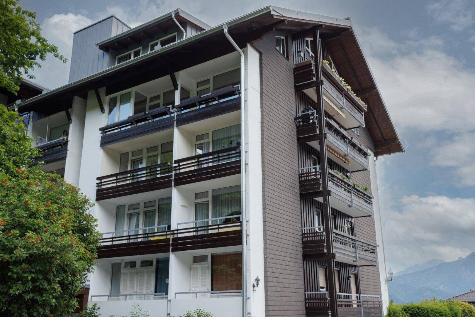 Mehrstöckiges Gebäude im alpinen Stil mit zahlreichen Balkonen und Blick auf die Berge.