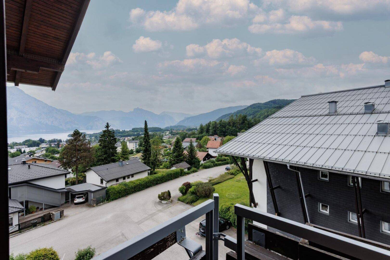 Panoramablick vom Balkon auf den See, die umliegenden Berge und die Wohnsiedlung.