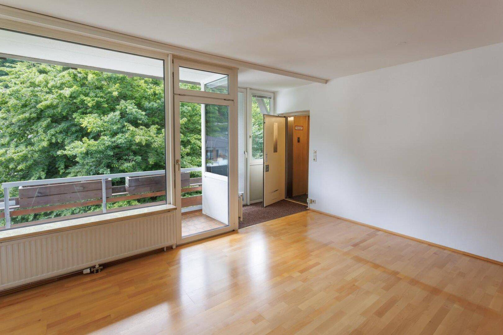Helles Wohnzimmer mit Parkettboden, großen Fenstern und Zugang zu einem kleinen Balkon.
