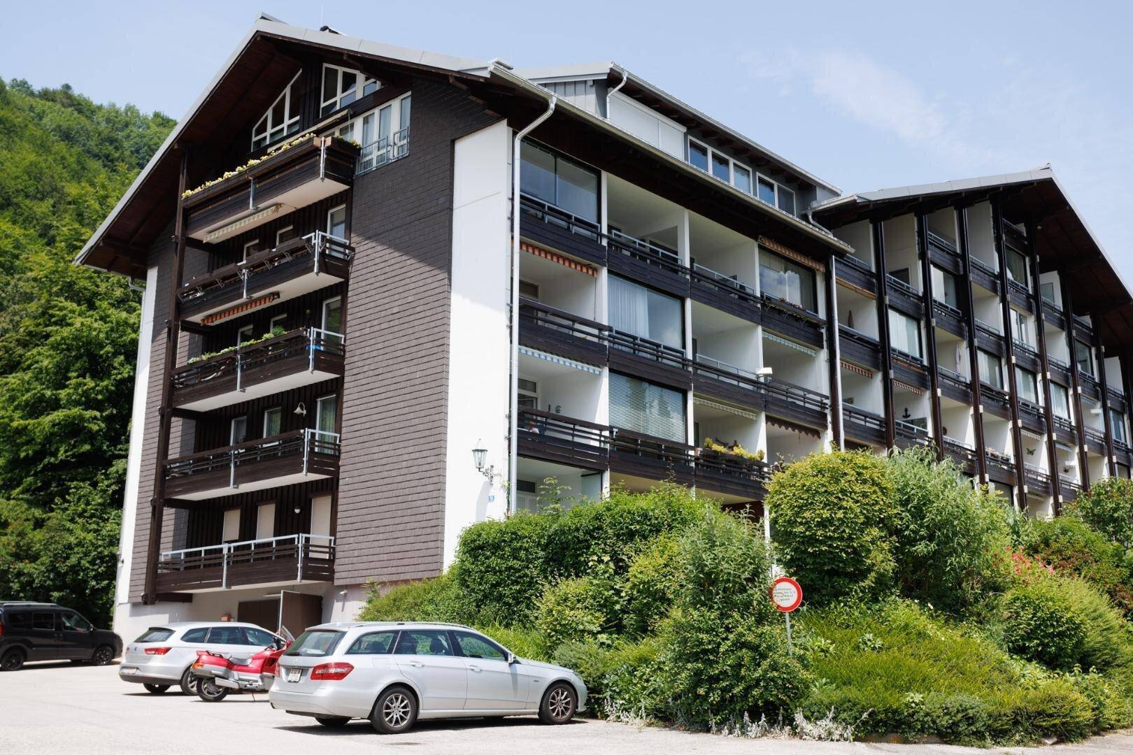 Gebäudekomplex im alpinen Stil mit Parkplätzen und grüner Umgebung an einem sonnigen Tag.