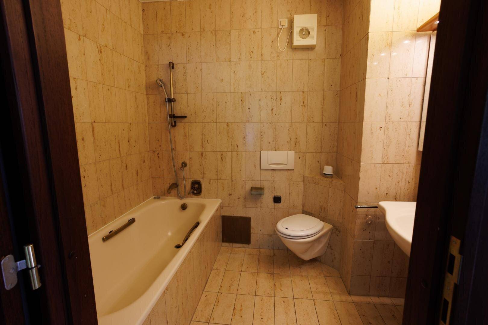 Badezimmer mit beigefarbenen Fliesen, Badewanne, wandhängendem WC und Waschbecken.