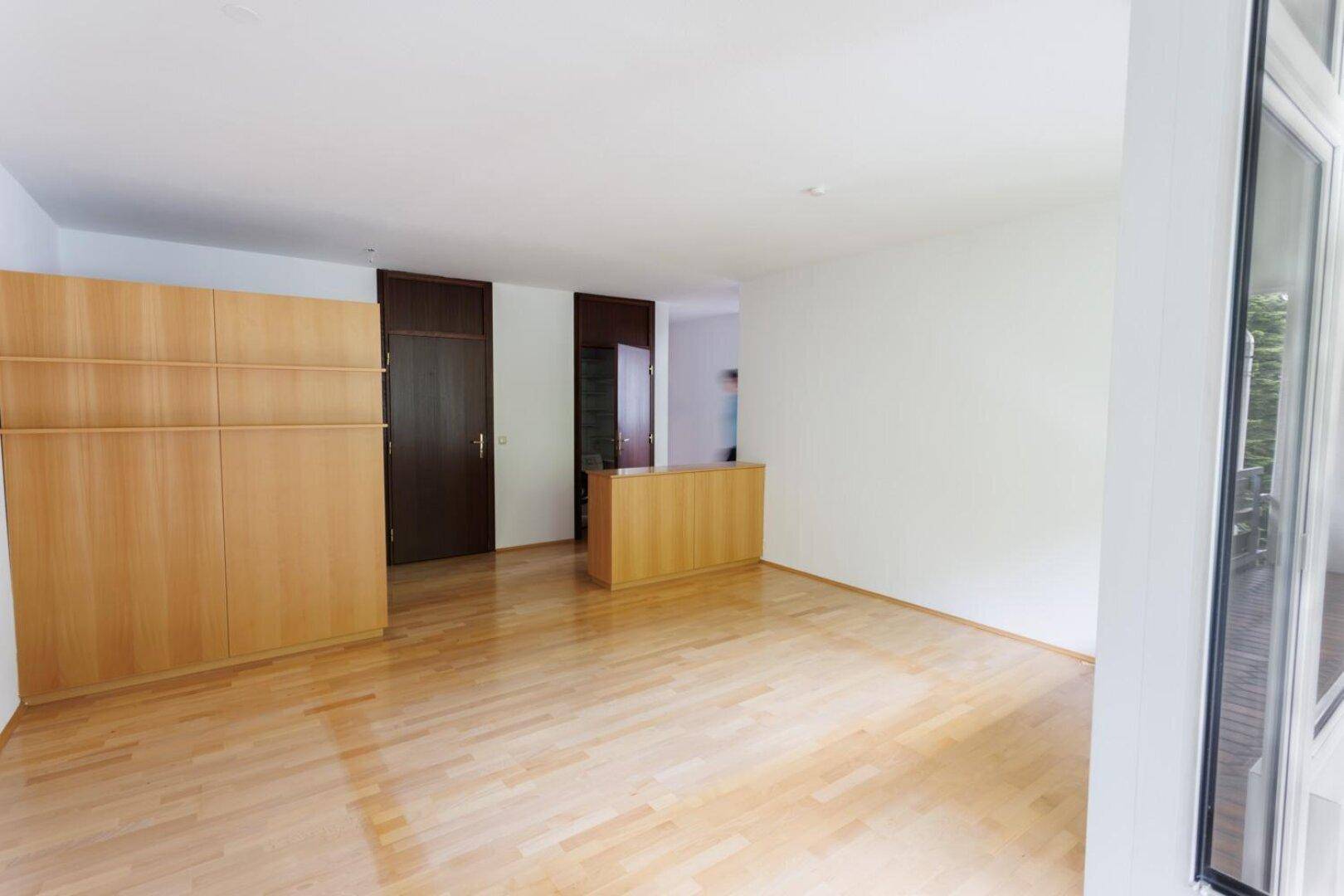 Heller Raum mit Holzparkett, weißen Wänden und integrierten Holzschränken.