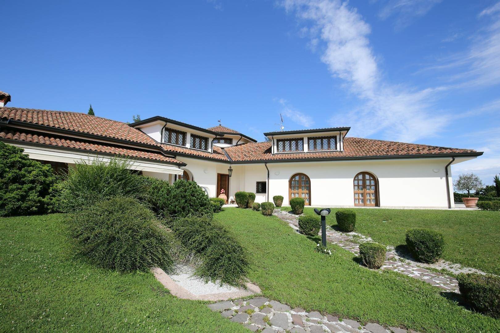 Vorderansicht der Villa mit gepflegtem Garten, Steinweg und üppiger Bepflanzung.