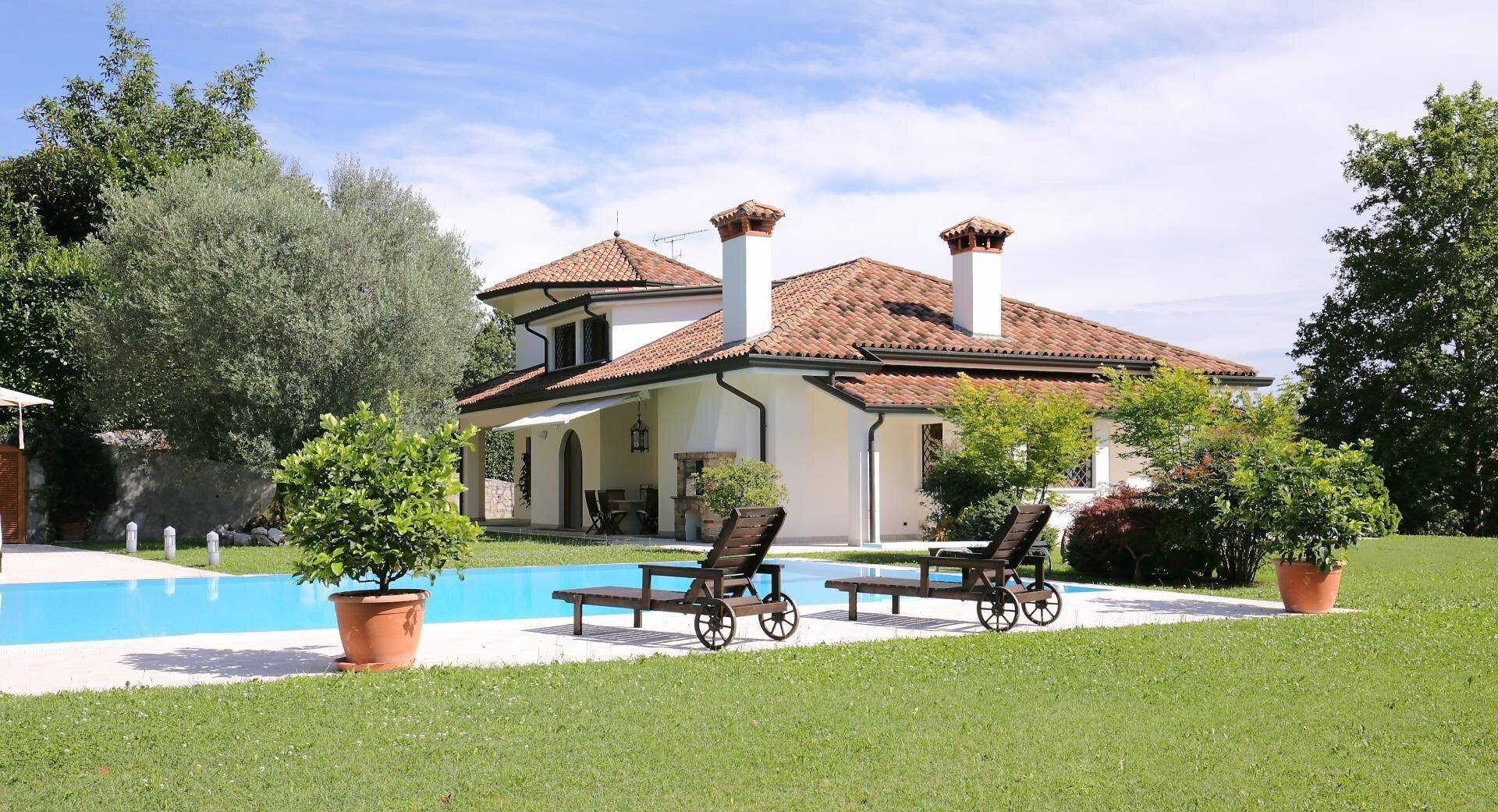 Weitläufiger Gartenbereich mit großem Pool, Liegestühlen und der Villa im Hintergrund.