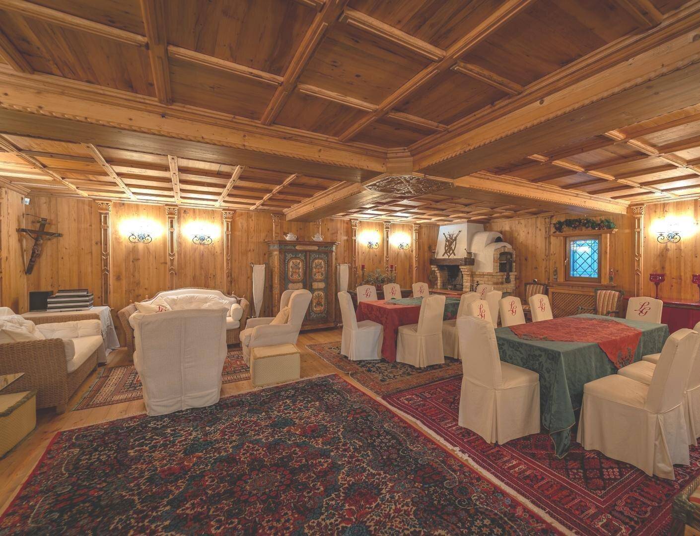 Großer Raum mit holzgetäfelten Wänden und Decken, mehreren Tischen und einem Kamin.