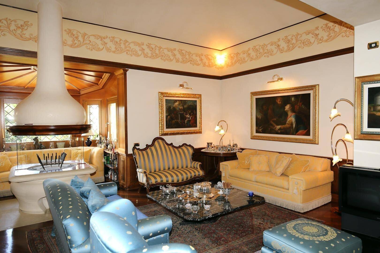 Luxuriöses Wohnzimmer mit opulenten Möbeln, Kamin und kunstvollen Deckenverzierungen.