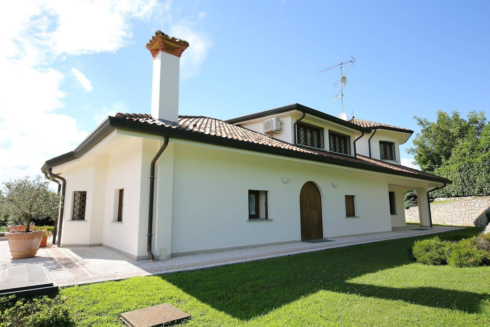 Seitenansicht der Villa mit weißer Fassade, Terrakottadach und Schornstein.