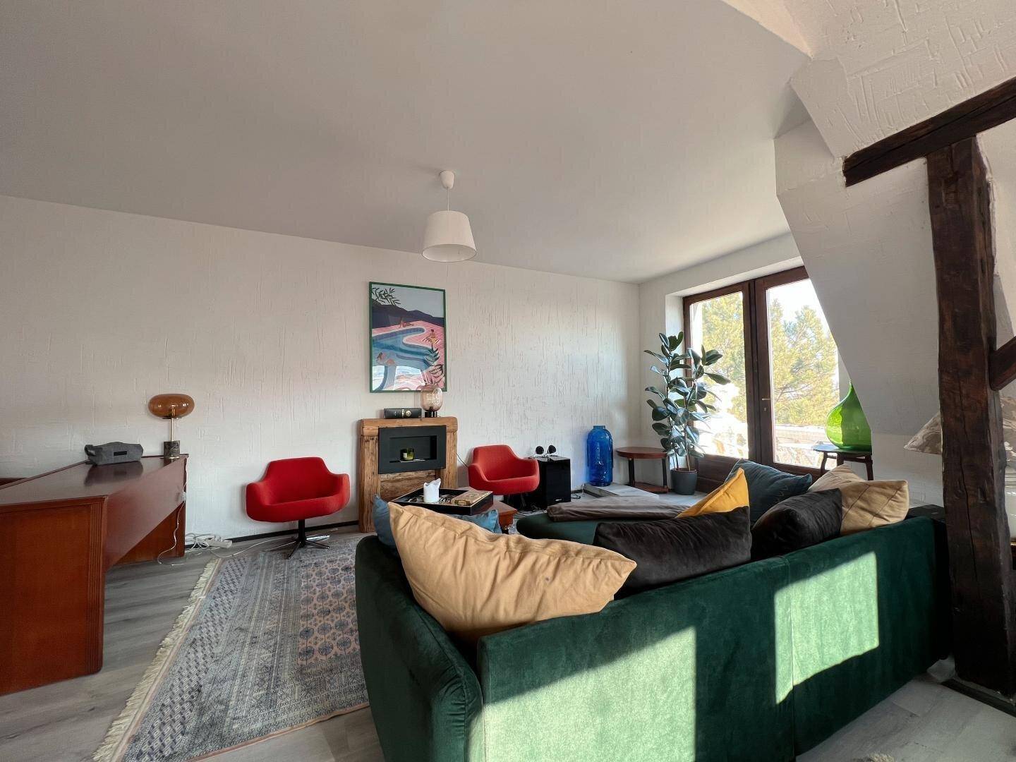 Helles Wohnzimmer mit grünem Sofa, roten Akzentstühlen und einem modernen Kamin unter Dachschrägen.