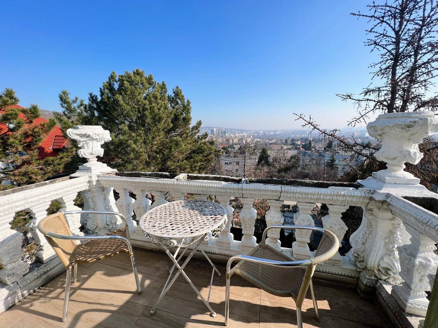 Balkon mit kunstvollem Geländer, kleinem Tisch und Stühlen, bietet einen weiten Stadtblick.
