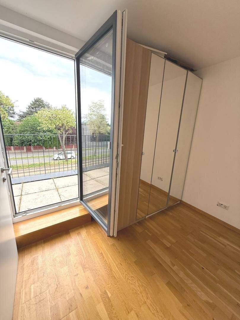 Schlafzimmer mit Holzboden, großen Fenstern und Blick auf die Straße.