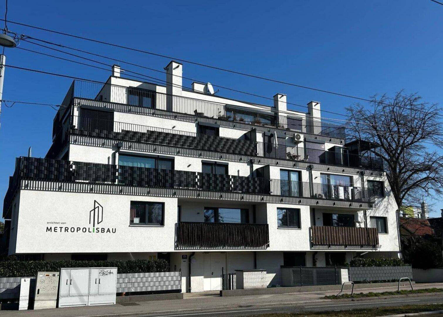 Modernes Mehrfamilienhaus mit weißer Fassade und mehreren Balkonen.
