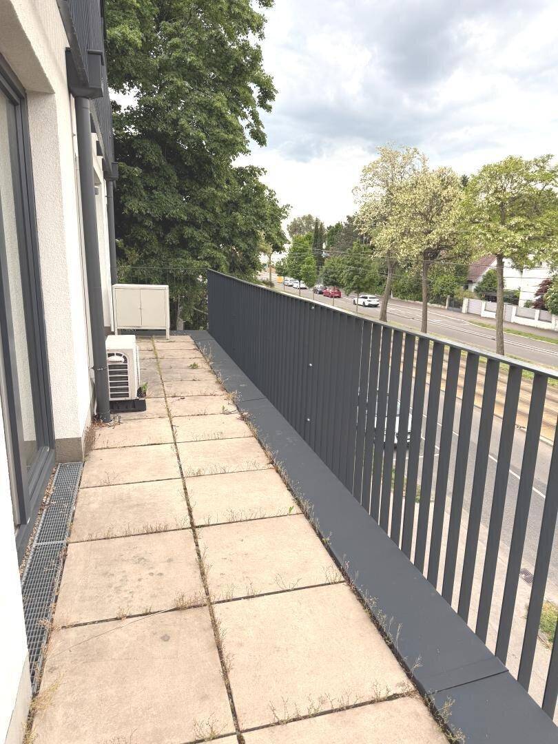 Langer Balkon mit Fliesenboden und Blick auf die Straße und Bäume.