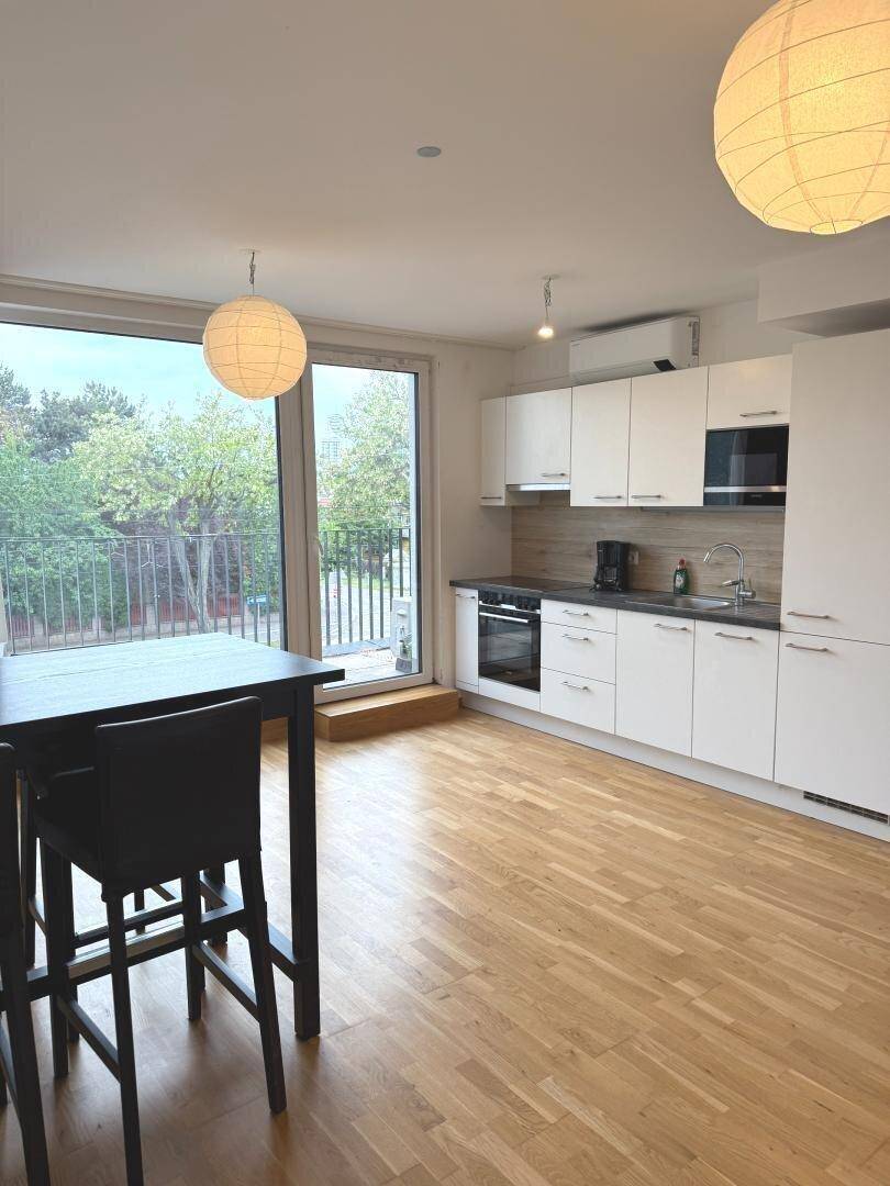 Moderne Einbauküche mit weißen Schränken, Holzboden und Zugang zum Balkon.