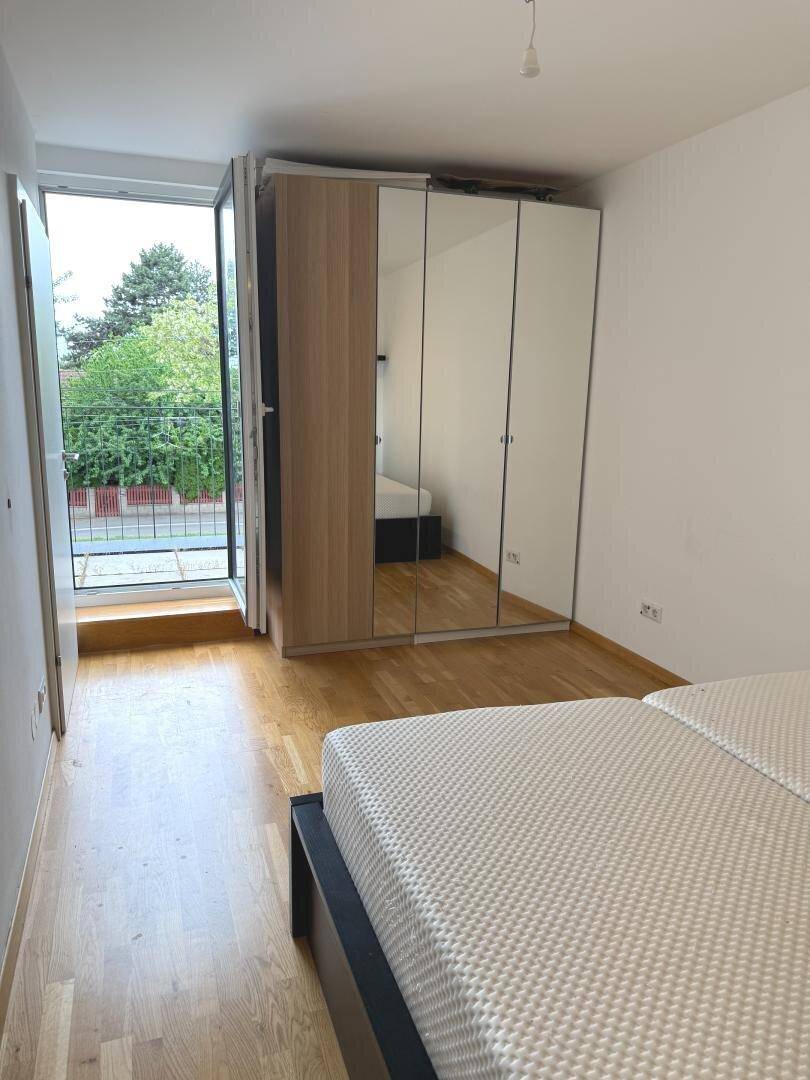 Schlafzimmer mit Holzboden, Spiegelschrank und Zugang zu einem französischen Balkon.