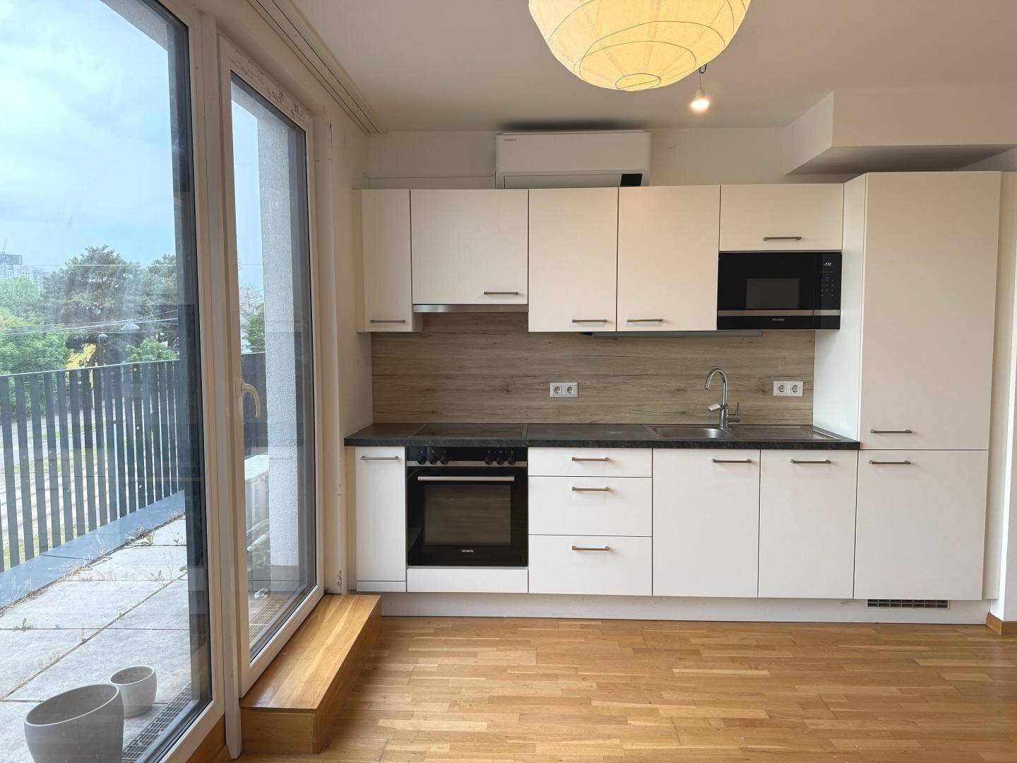 Helle Küche mit weißen Schränken, dunkler Arbeitsplatte und Blick auf den Balkon.