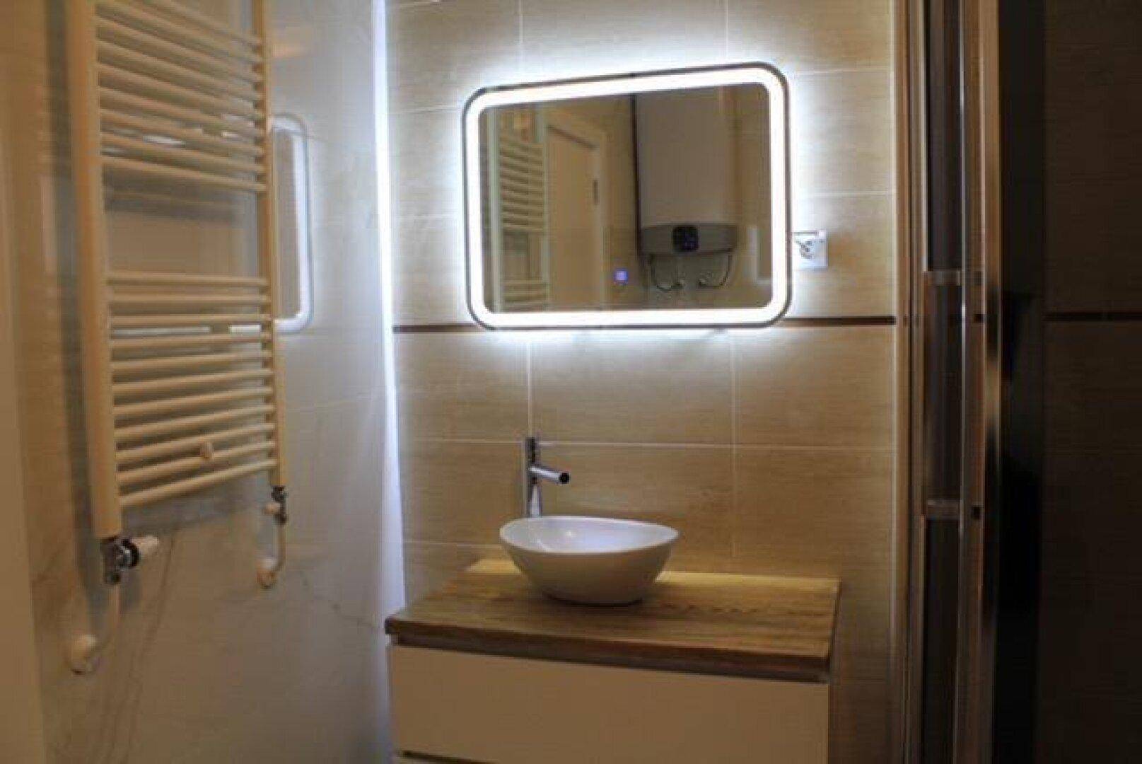 Modernes Badezimmer mit Aufsatzwaschbecken, Holzwaschtisch und beleuchtetem Spiegel.