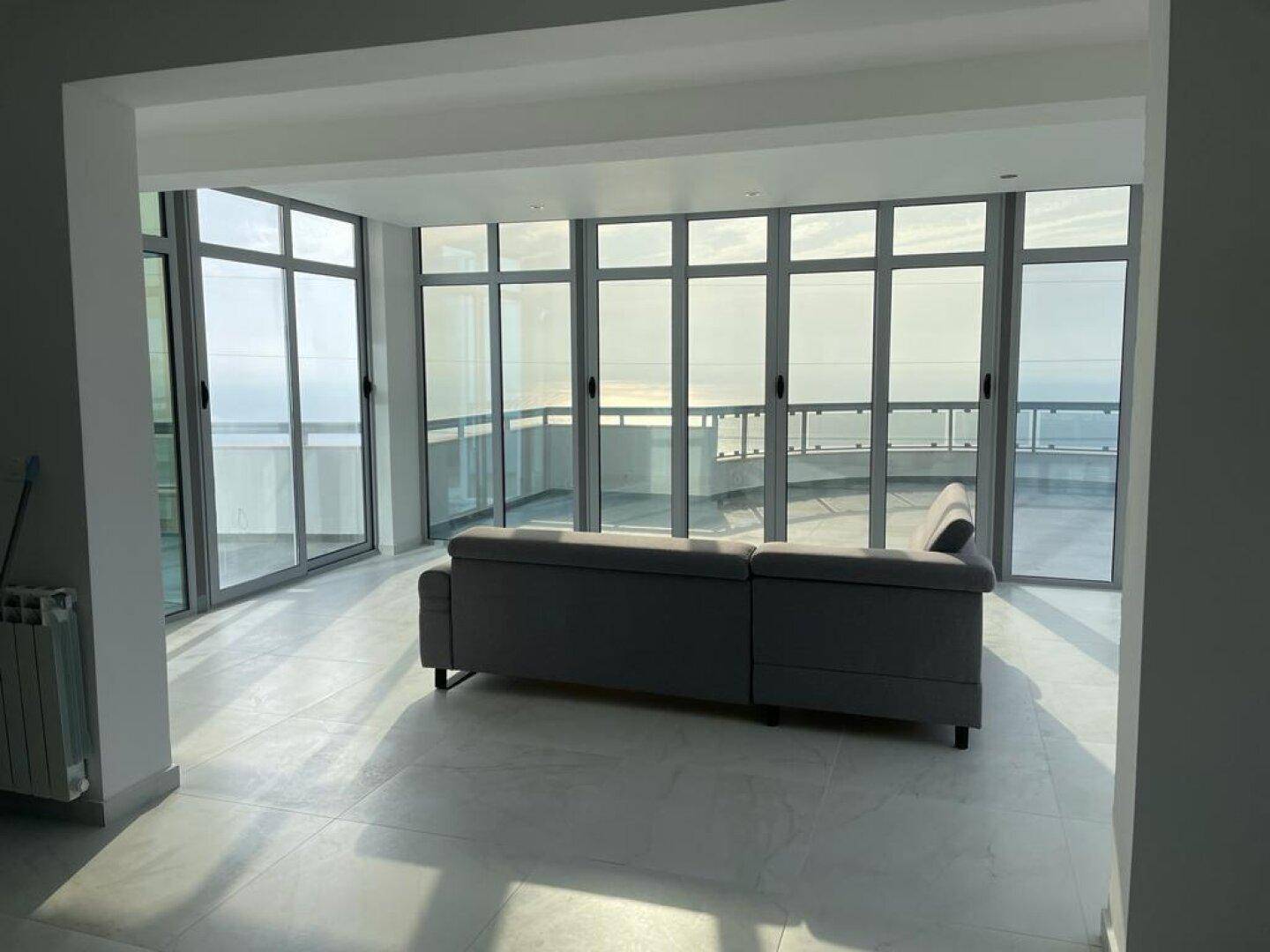 Modernes Wohnzimmer mit Sofa und Panoramafenstern, die einen weiten Meerblick bieten.