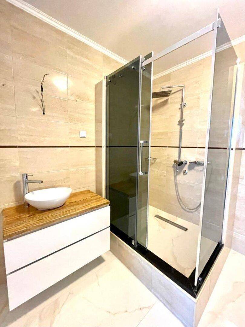 Modernes Badezimmer mit großer Duschkabine, Aufsatzwaschbecken und Holzwaschtisch.
