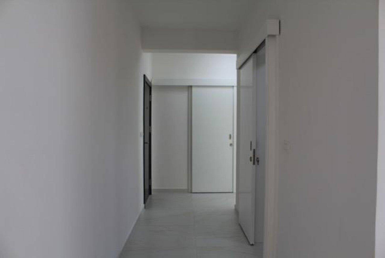 Heller Flur mit schlichten weißen Wänden und modernen Schiebetüren.