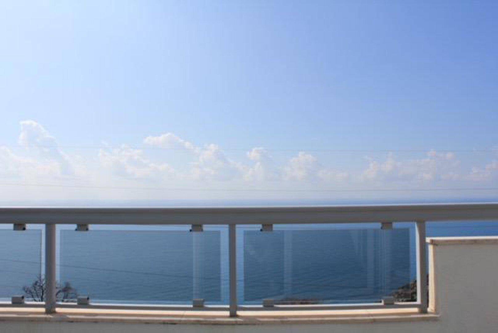 Blauer Himmel über dem weiten Meer, genossen von einem Balkon mit modernem Glasgeländer.