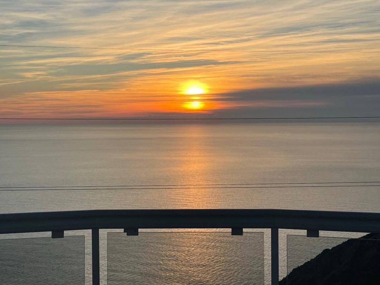 Spektakulärer Sonnenuntergang über dem Meer, gesehen von einer privaten Terrasse mit Glasgeländer.