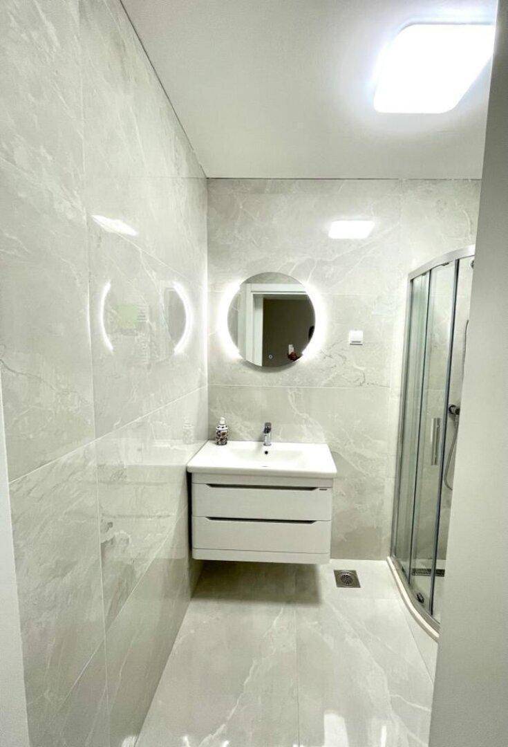 Elegantes Badezimmer mit modernem Waschtisch, beleuchtetem Spiegel und Duschkabine.