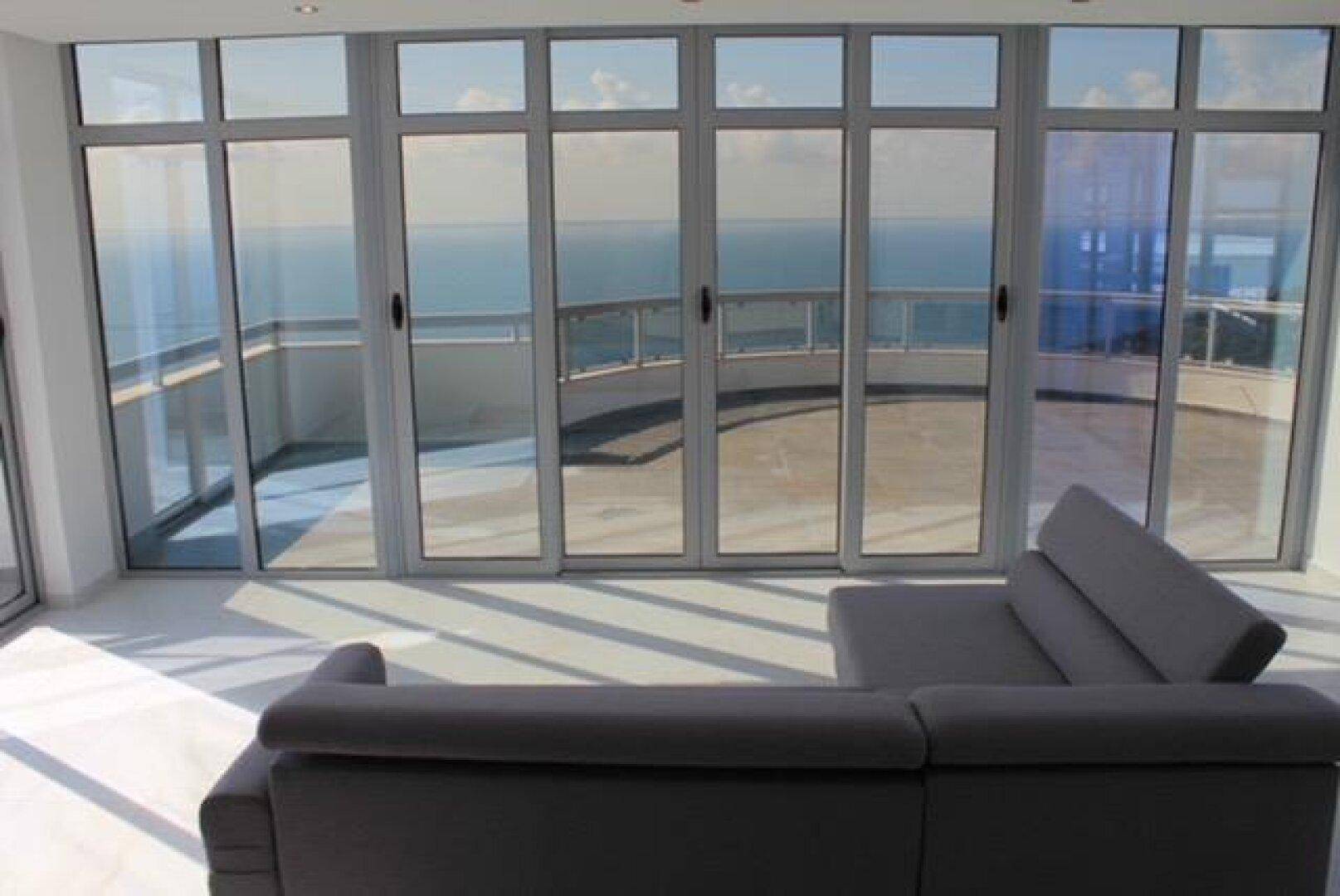 Modernes Wohnzimmer mit Ecksofa und Panoramafenstern, die einen weiten Meerblick bieten.